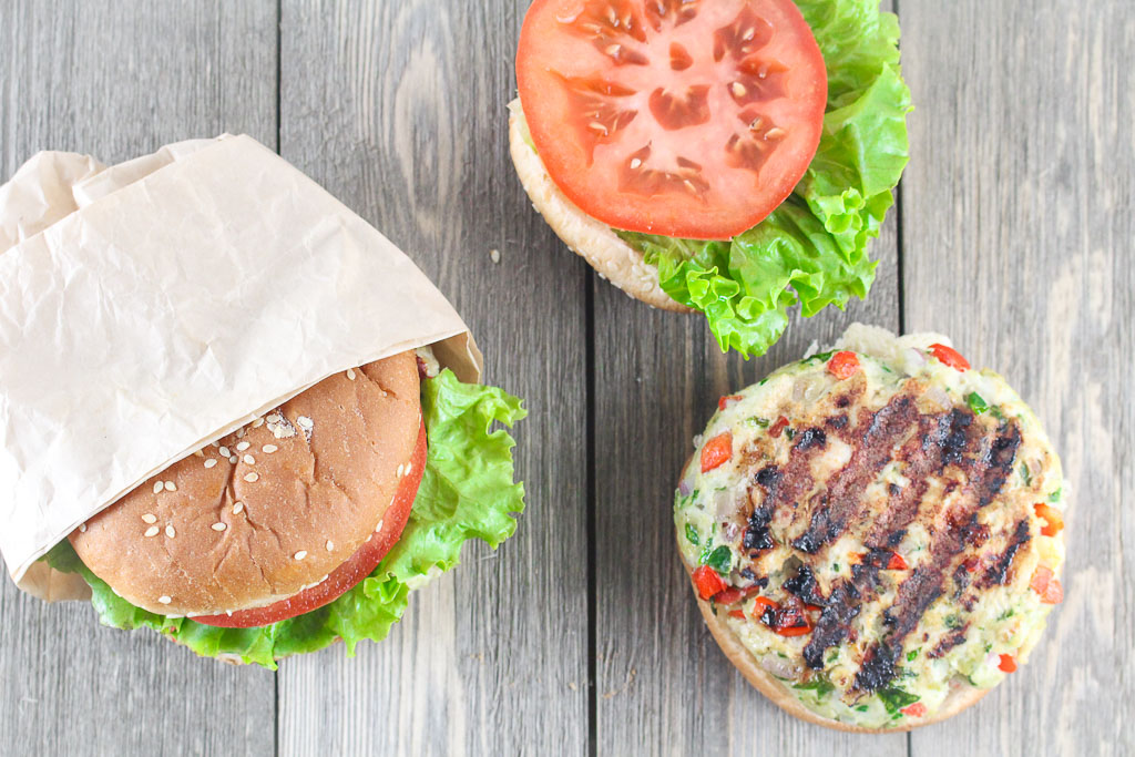 open-faced burger on a sesame seed bun with lettuce and tomato in a brown wrapper