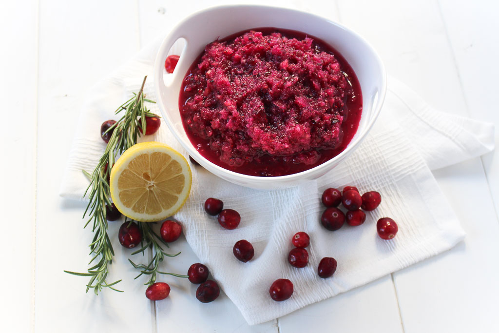 a small bowl of cranberry relish next to lemon, garnish, and single cranberries