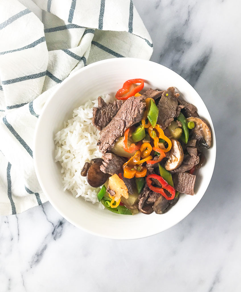 Beef stir fry in a white bowl with white rice