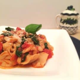 Tortellini with tomatoes, white beans, & spinach on a white plate
