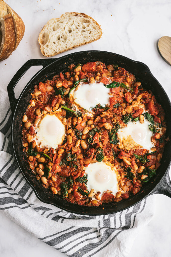 cast iron skillet with white bean shakshuka with a piece of bread