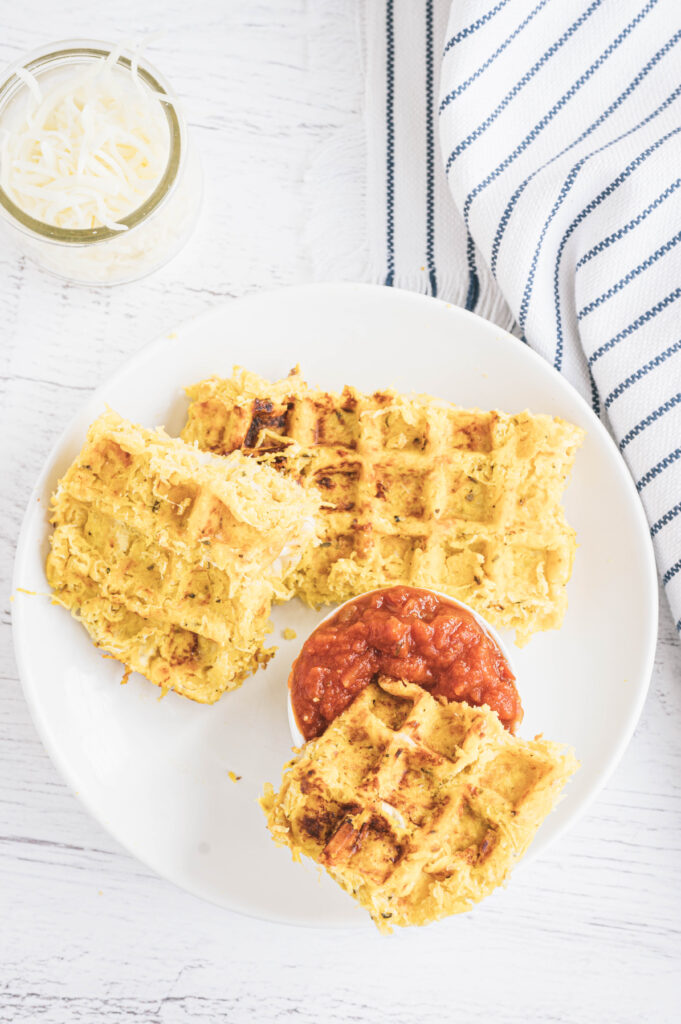 Spaghetti Squash Waffle Grilled Cheese on a white plate, one piece dipped in marinara sauce