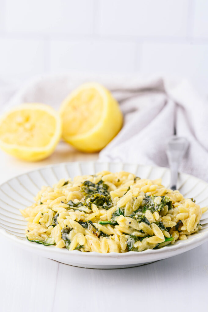 creamy lemon orzo with spinach on a plate with lemons in the background