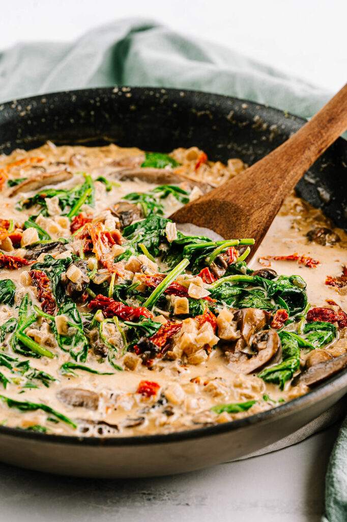 creamy tuscan chicken in a large skillet with a wooden spoon. 